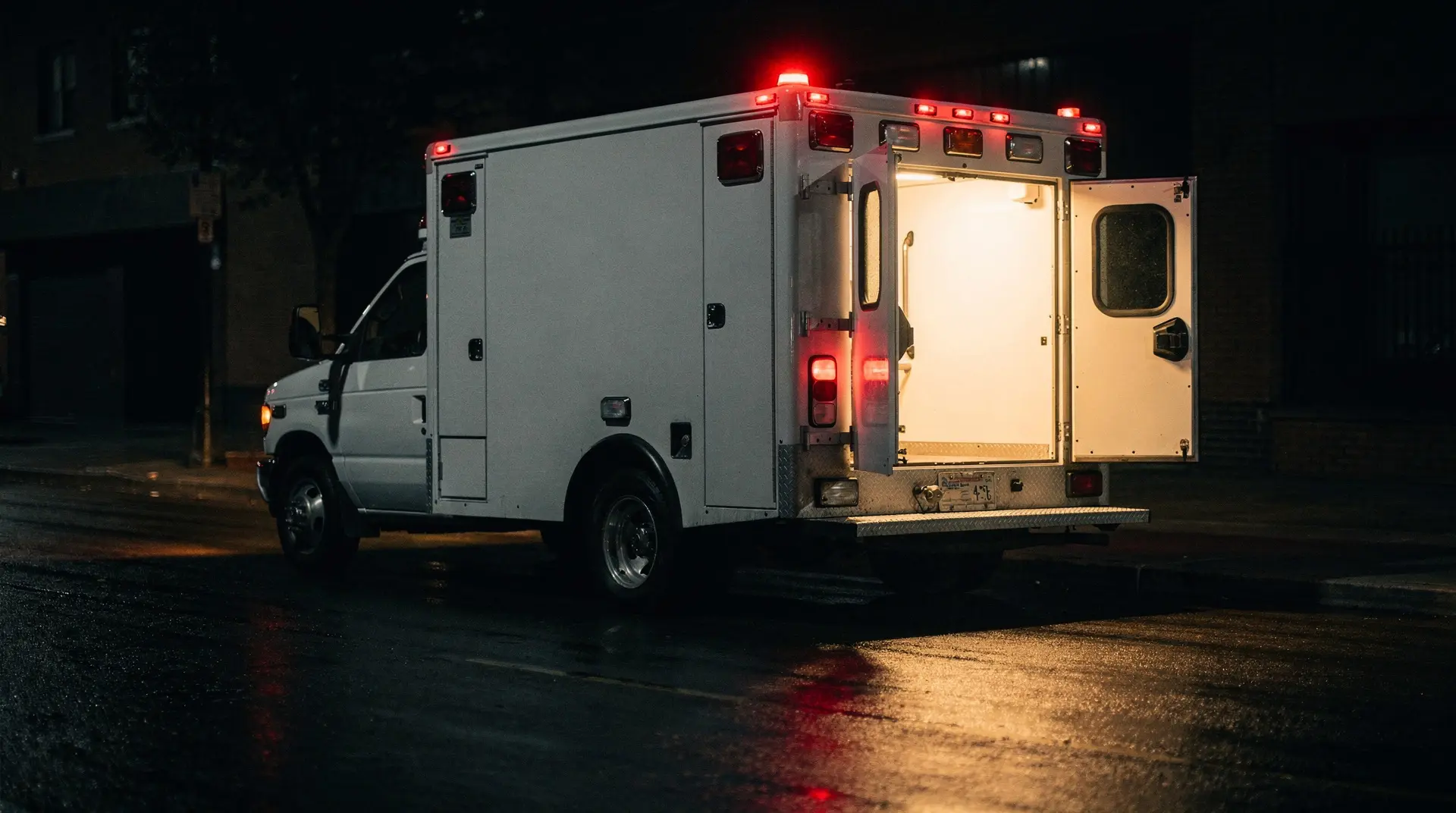An ambulance at night with its rear doors open, interior light spilling onto the street